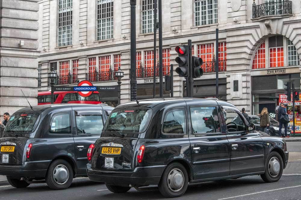 two black cabs waiting on a traffic light in london