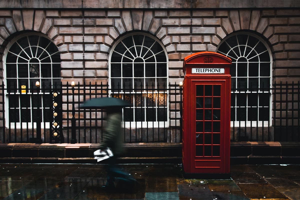 manwith-umbrella-walking-in-front-of-a-red-telephone-cabin