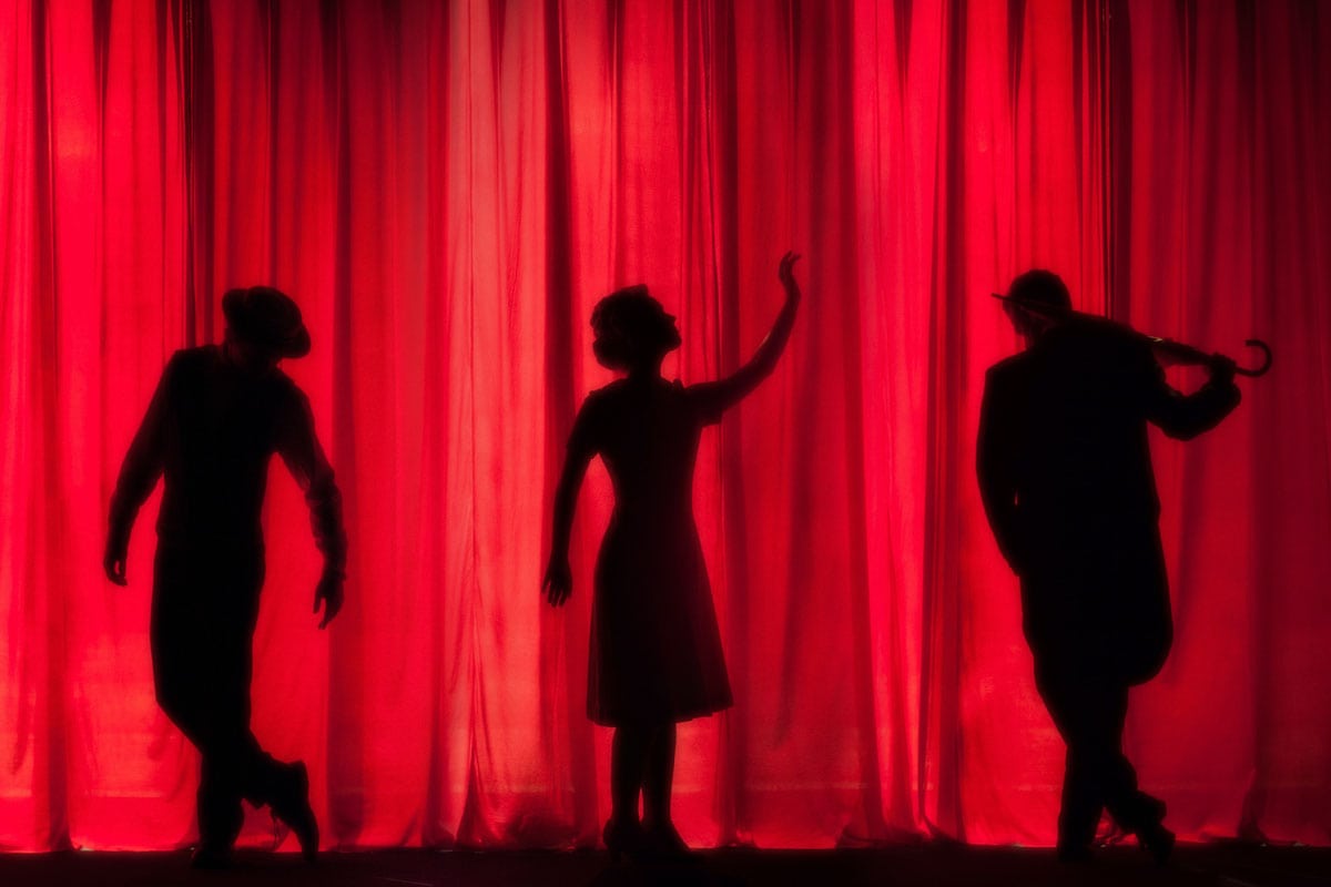 silhouettes-of-three-actors-behind-a-red-curtain