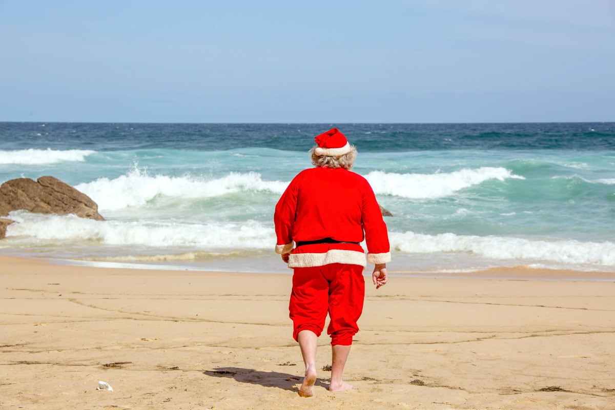 man-in-santa-outfit-walking-on-the-beach