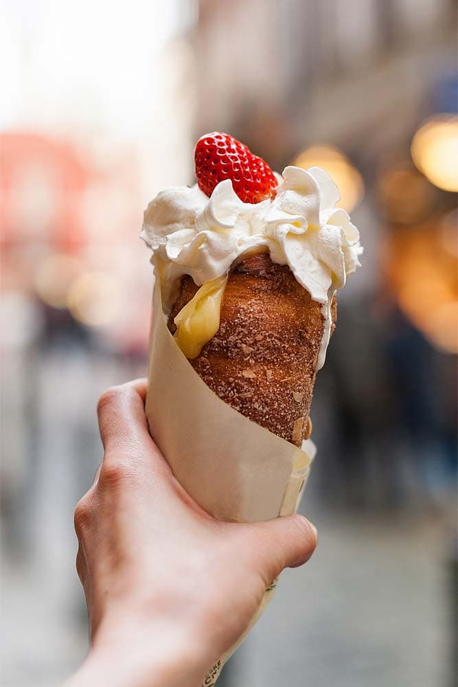 womans-hand-holding-trdelnik-with-cream-and-strawberry